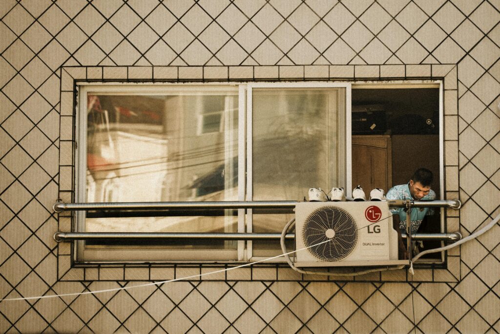 Man looks outside a window with an LG air conditioner unit visible, creating a reflective effect.